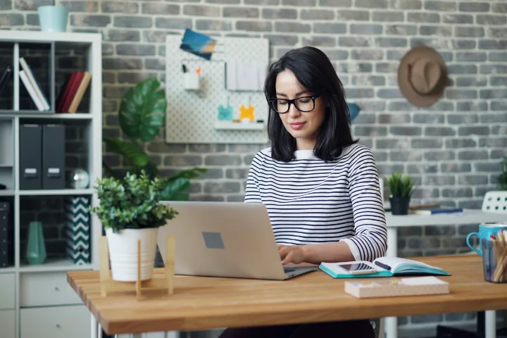 Woman in glasses typing on a laptop at a wooden desk